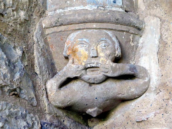 Un chapiteau décoré de la tête d'un personnage tirant la langue et  écartant sa bouche avec les doigts