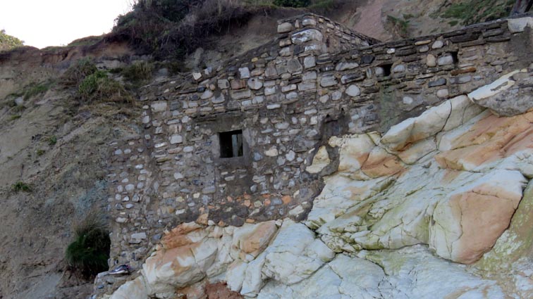 Un petit bâtiment en maçonnerie plus ou moins en ruines qui se trouve accroché en pied de falaise